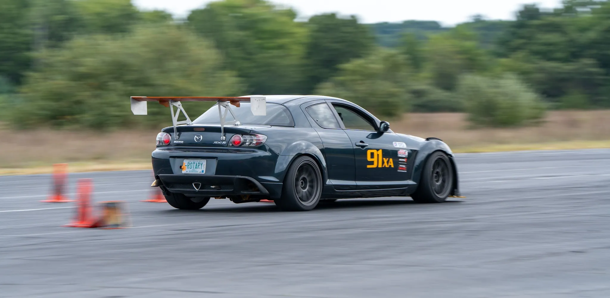 Mazda RX8 on track with trunk mounted wing uprights, rear 3/4 view